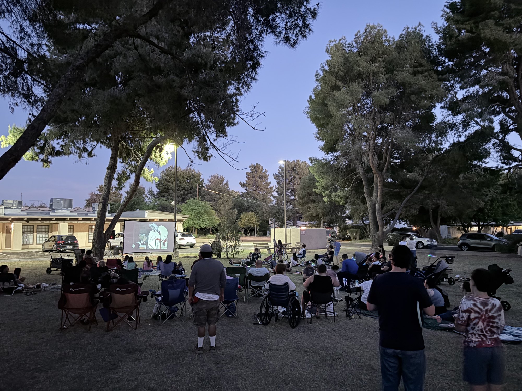 Neighbors watching 101 Dalmatians on an outdoor screen at dusk in the park